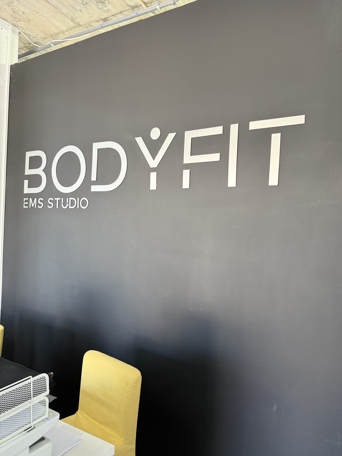Logo BODYFIT EMS Studio em letras brancas sobre parede escura no estúdio.